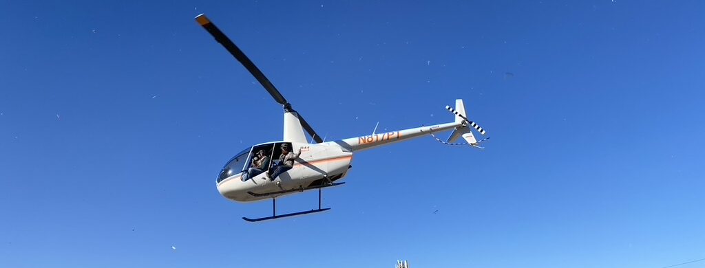 a thrilling aerial view captures a sleek helicopter soaring above expansive texas landscapes, with the focus on a rugged terrain dotted with wild boar, highlighting the intensity and strategy of aerial hog hunting under state regulations.