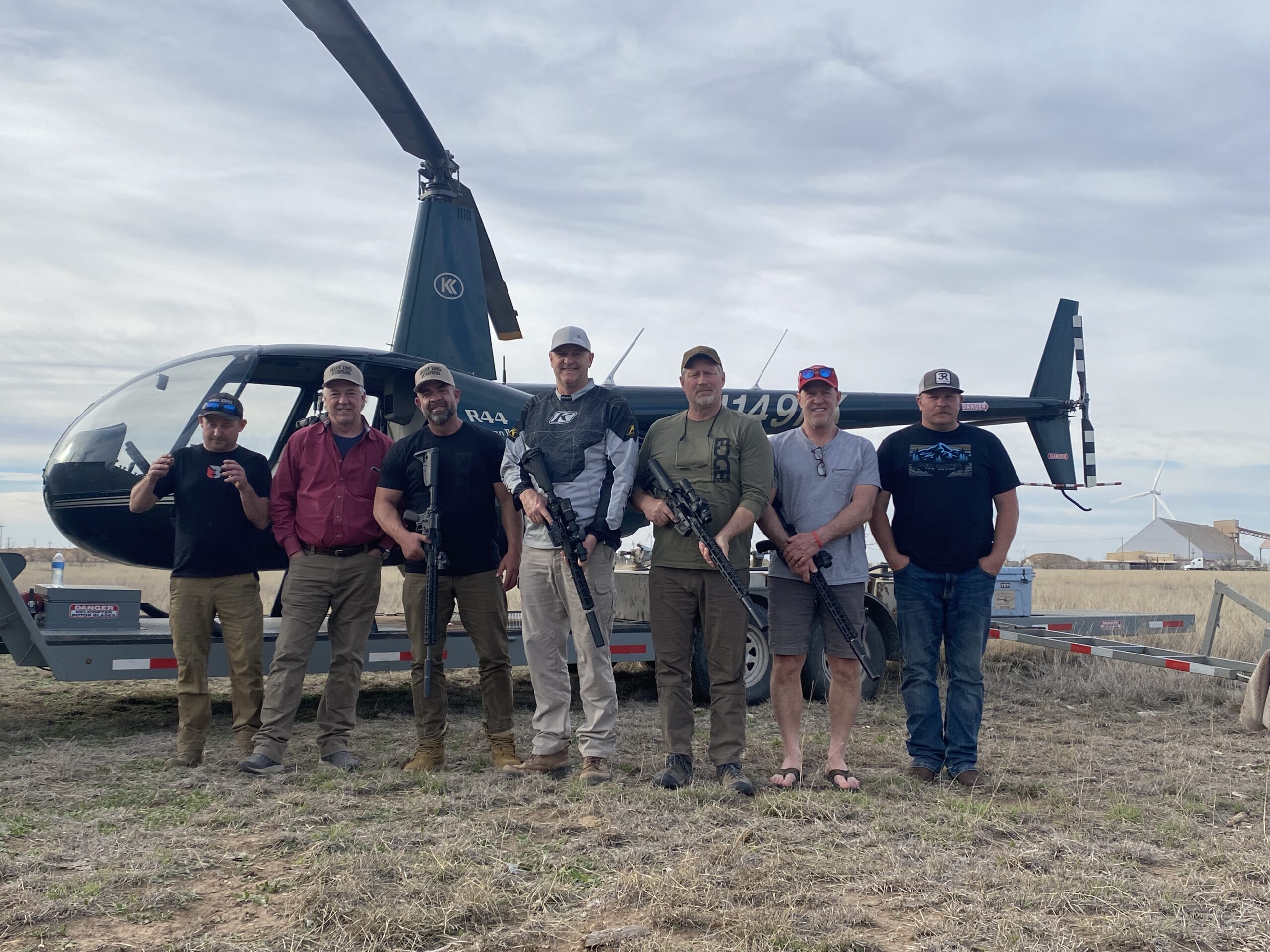 a thrilling aerial view captures a sleek helicopter soaring above expansive texas landscapes, with the focus on a rugged terrain dotted with wild boar, highlighting the intensity and strategy of aerial hog hunting under state regulations.