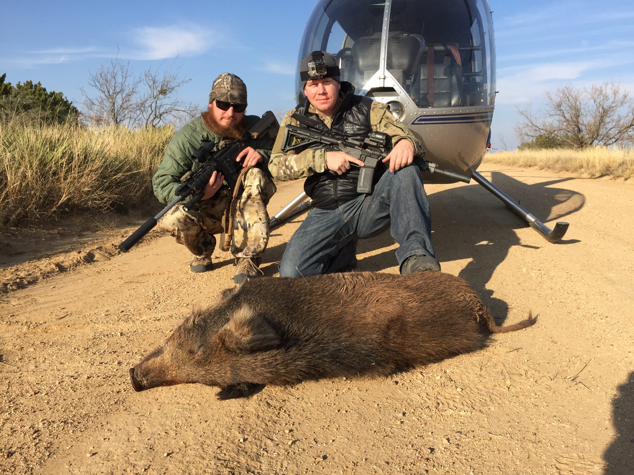 a dynamic aerial view captures a helicopter in action during a coordinated hog hunt over a sprawling texas landscape, showcasing the strategic approach to feral hog management while highlighting the contrast between technology and the rugged terrain below.