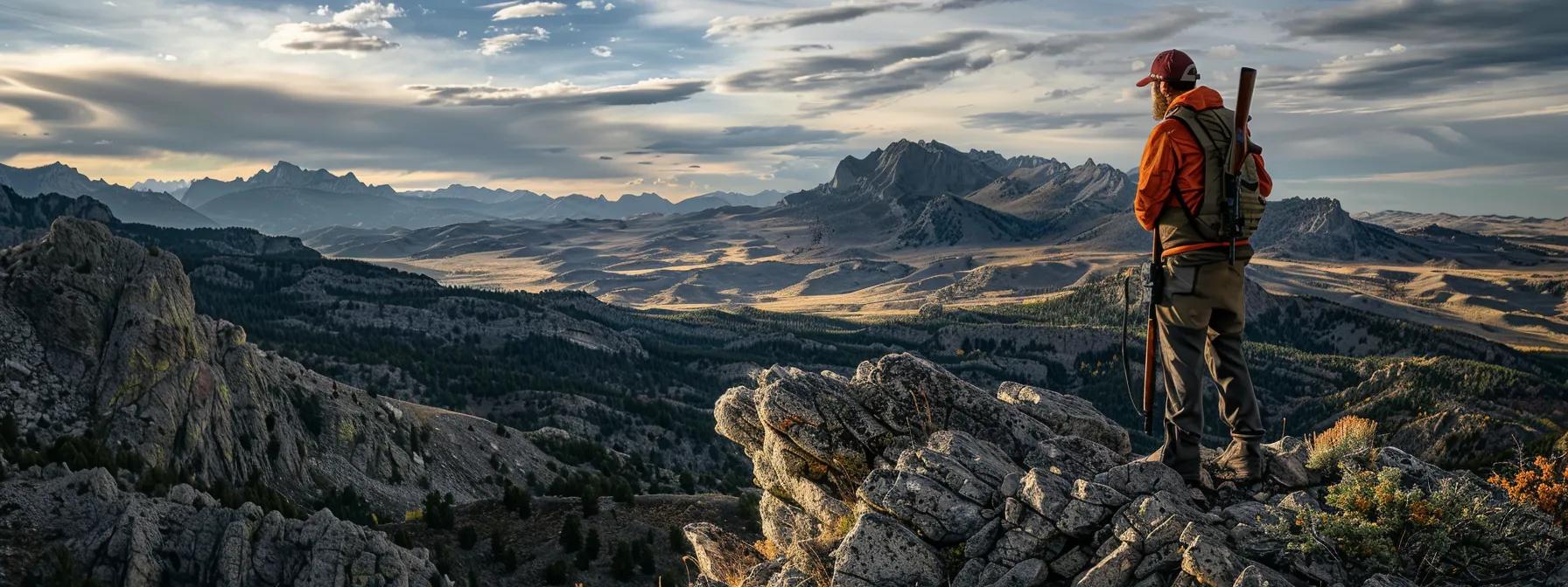 a determined hunter clad in rugged outdoor gear stands confidently on a rocky outcrop against the dramatic backdrop of wyoming's mountainous terrain, holding a rifle while observing the landscape, embodying the principles of ethical hunting practices in a clear and authoritative manner.